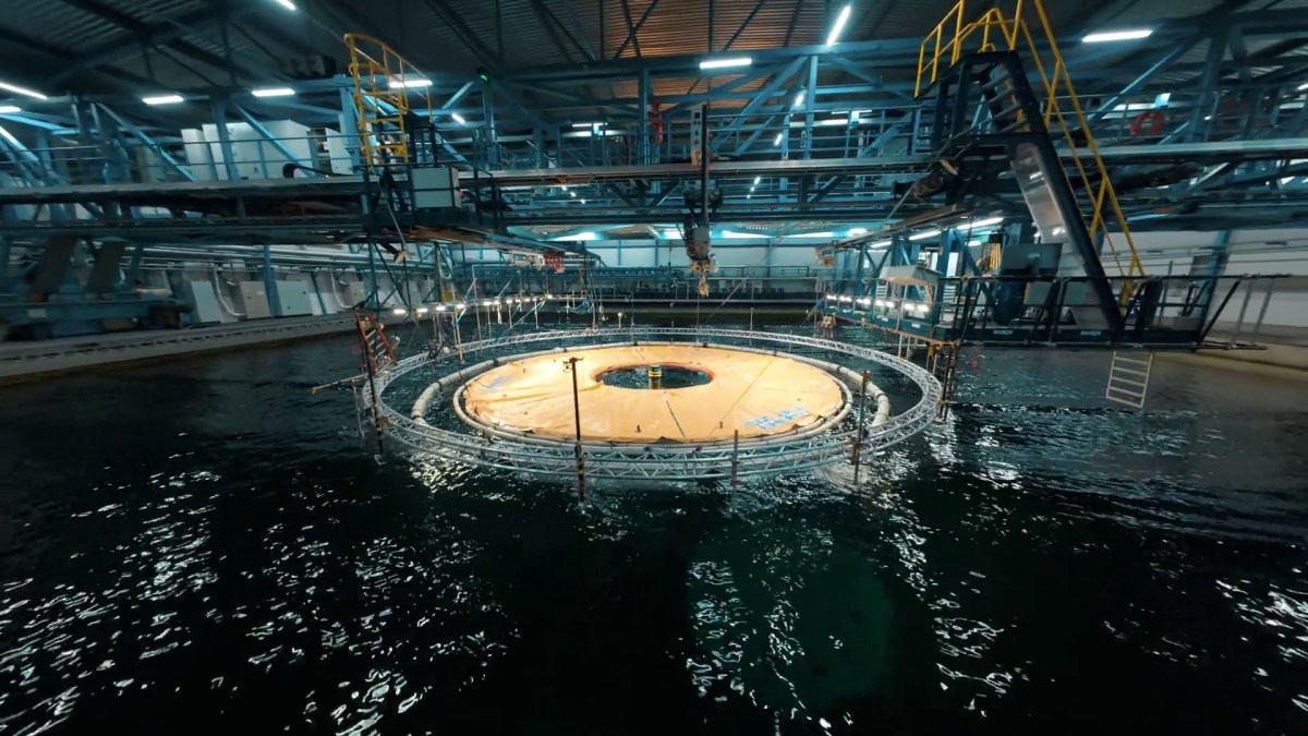 An orange plastic reservoir sits inside a wave tank in a testing facility.