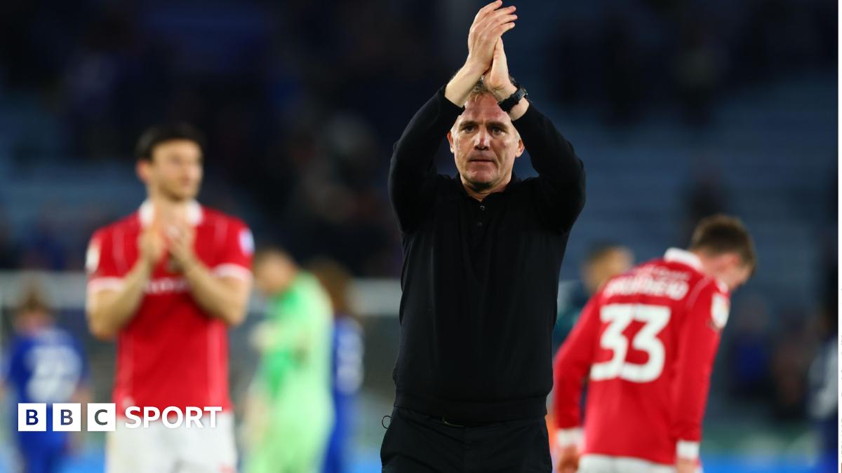 Manager Phil Parkinson, dressed in a black top and trousers, applauds supporters with Wrexham players behind him in the background