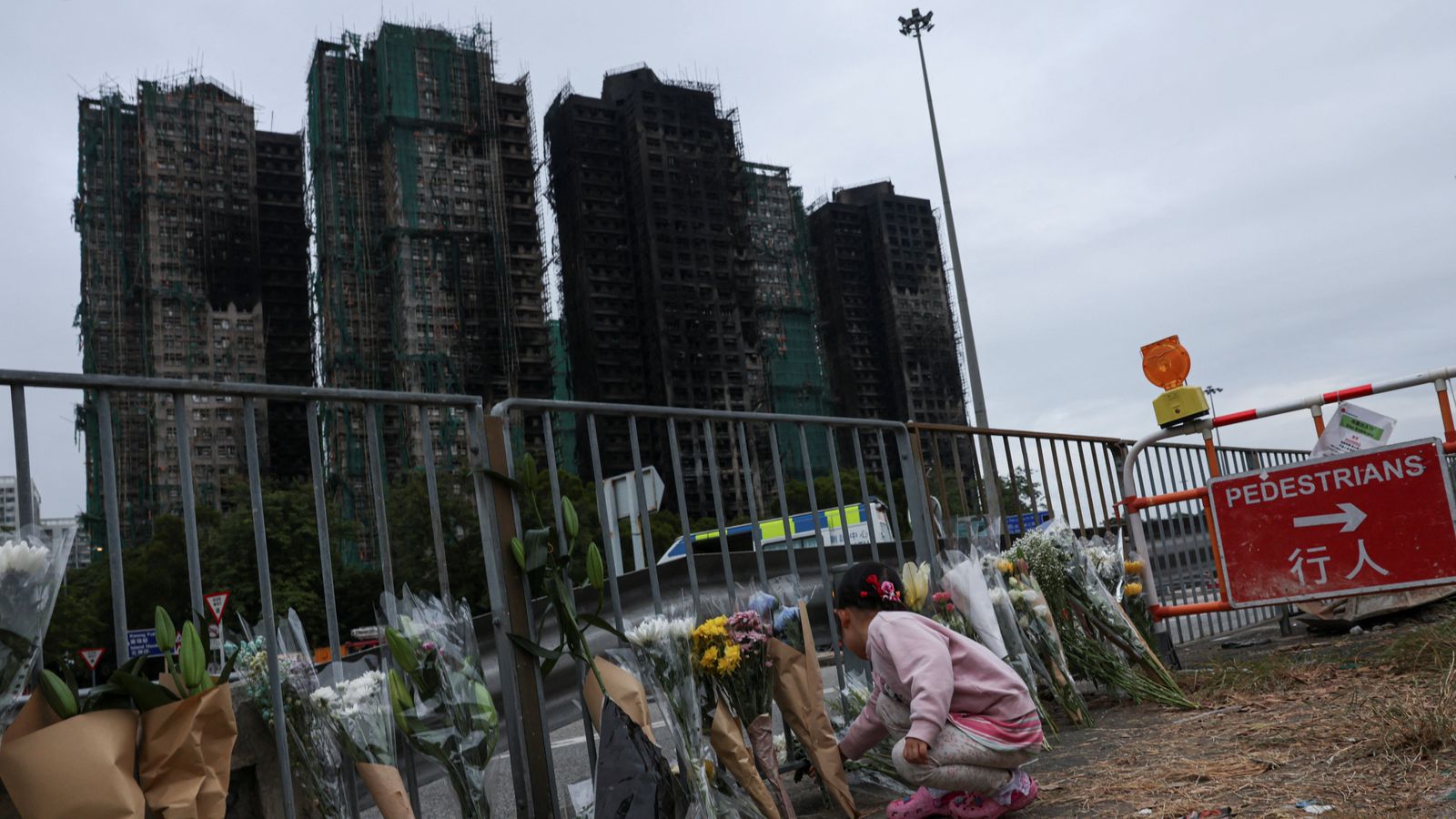 A girl places flowers in front of the fire-damaged residential blocks at Wang Fuk Court. Pic: Reuters