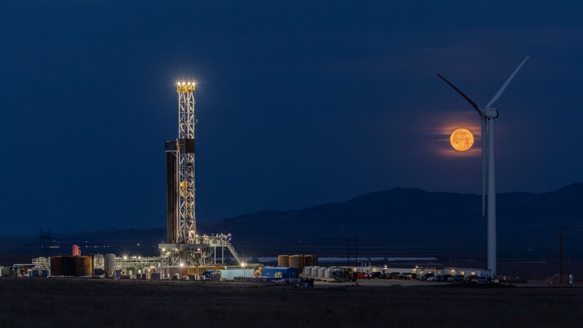 Fervo's drilling rig lit up at night with the moon rising in the background.